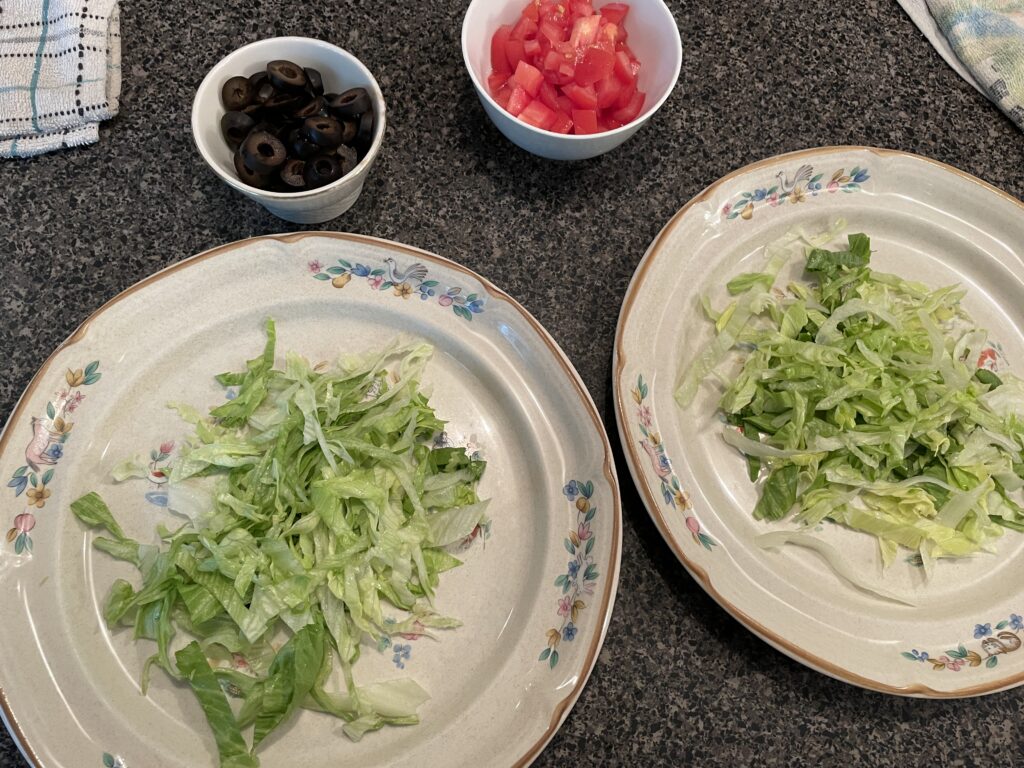 Diced tomatoes, sliced black olives, and shredded lettuce ready for plating