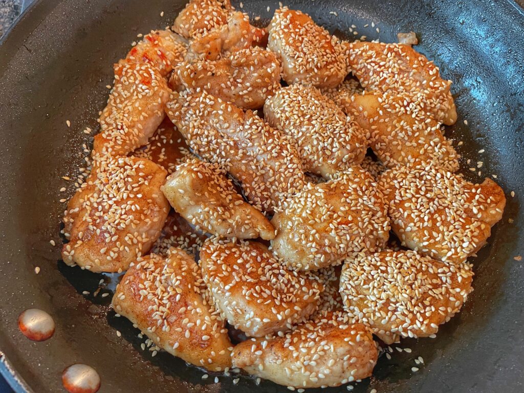 Sesame Chicken tenders in the pan coated with the sauce and sprinkled with sesame seeds