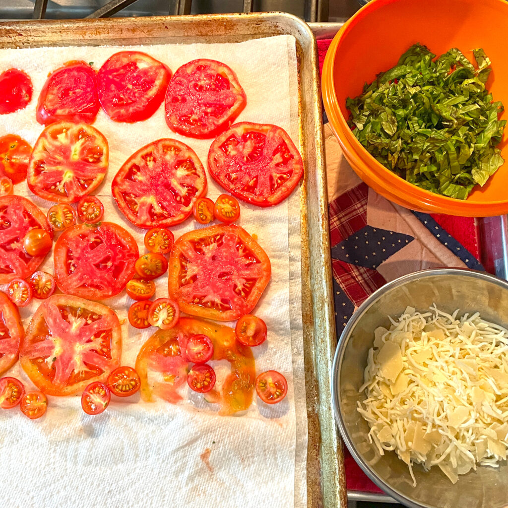 Sliced heirloom tomatoes, chiffonade of basil, and two parmesan cheeses ready to top the prebaked dough