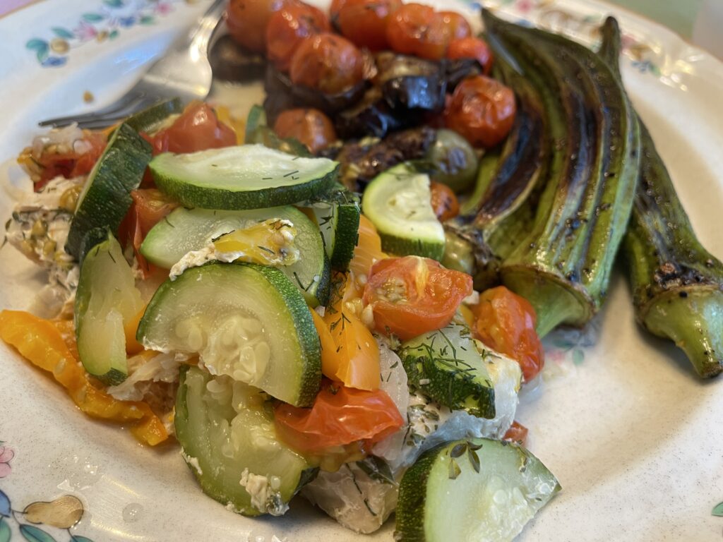 Mahi Mahi portion with vegetables and herbs, with a side of okra and eggplant and tomatoes