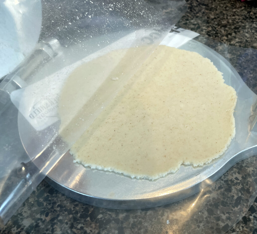 Pressed dough into tostada with plastic lifted up